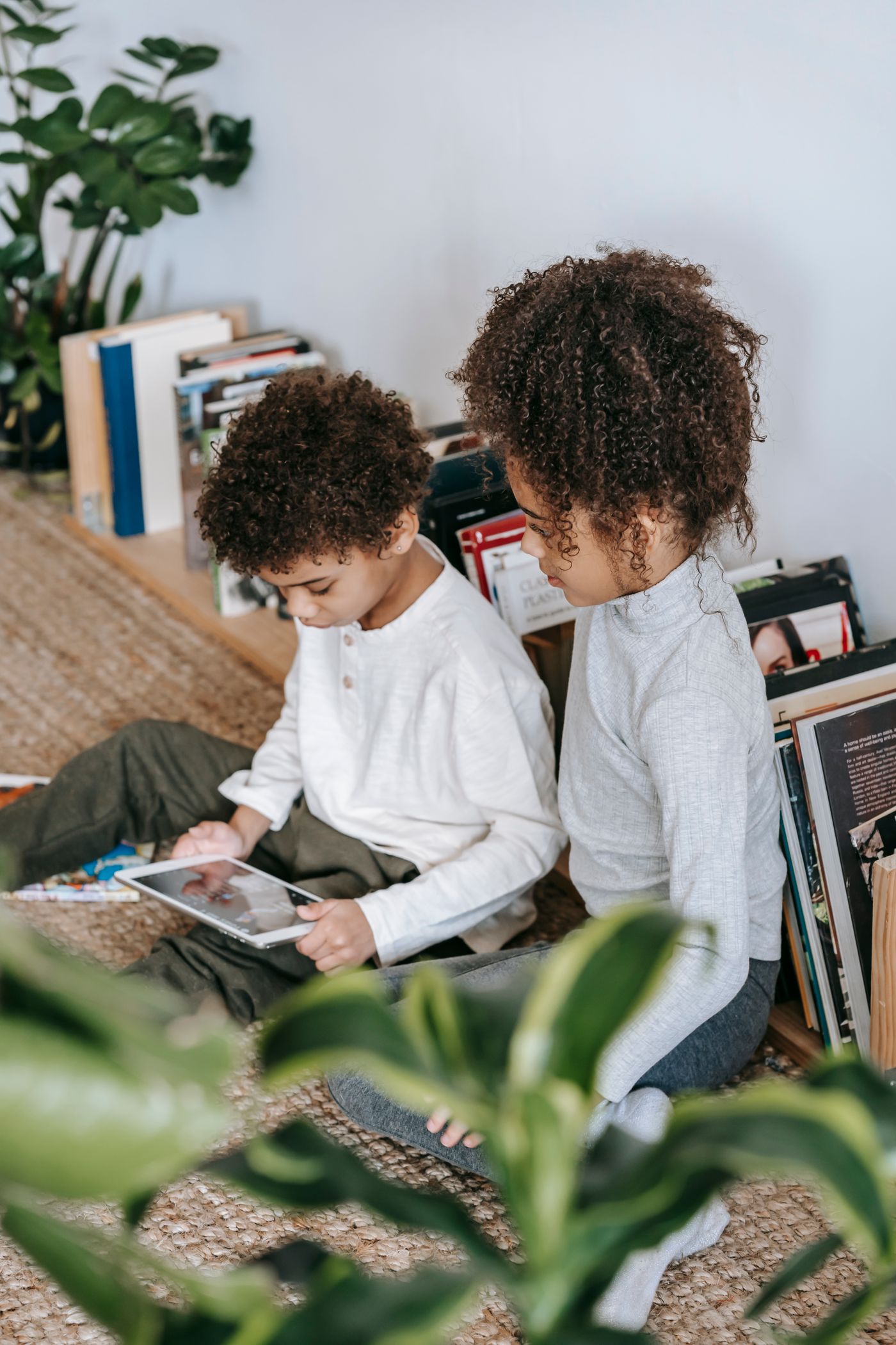 Two Black children exploring a tablet beside their books